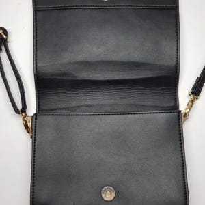 Puede incluir: Bolso bandolera rectangular negro con cierre de solapa y cierre magn&eacute;tico. El bolso tiene una correa larga y delgada y herrajes dorados. El interior es visible, revelando un compartimento espacioso. El bolso est&aacute; hecho de un material liso similar al cuero.