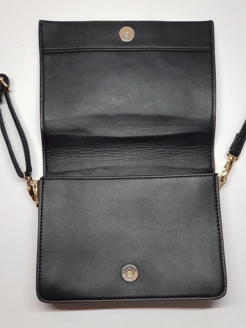 Puede incluir: Bolso bandolera rectangular negro con cierre de solapa y cierre magn&eacute;tico. El bolso tiene una correa larga y delgada y herrajes dorados. El interior es visible, revelando un compartimento espacioso. El bolso est&aacute; hecho de un material liso similar al cuero.
