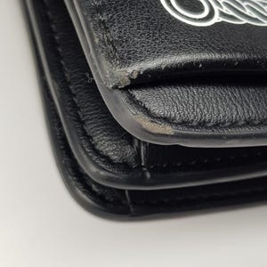 Puede incluir: Primer plano de un bolso de mano de cuero negro con un dise&ntilde;o de cadena blanca en la solapa. El bolso muestra signos de desgaste en los bordes. El bolso es probablemente un bolso de hombro o bandolera.