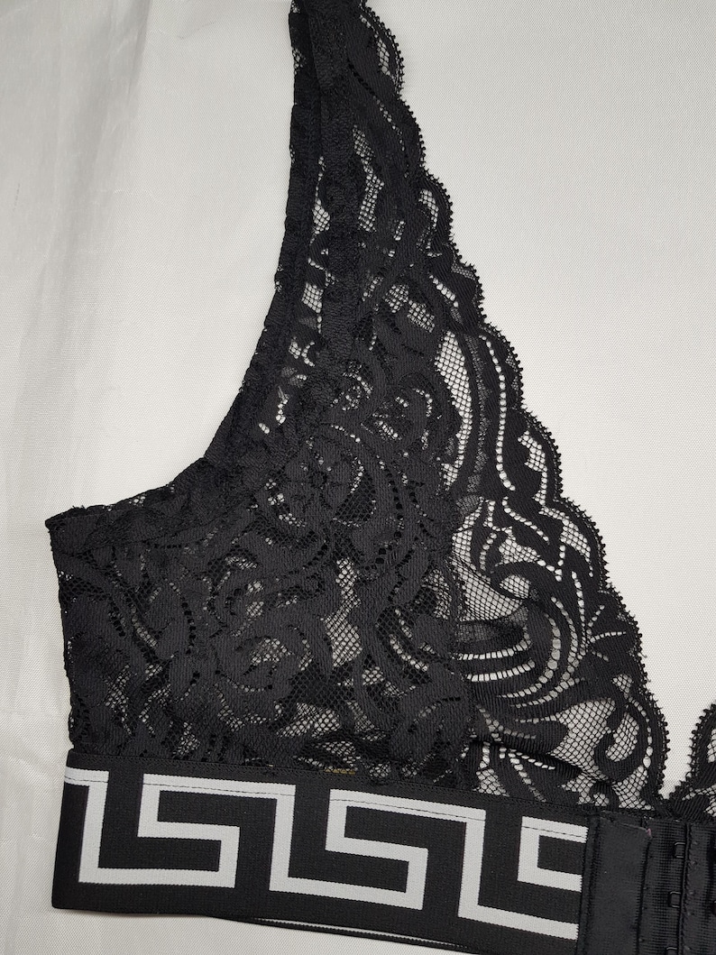 May include: Black lace bra with a decorative pattern. The bra features a wide band with a white and black geometric design. The bra has adjustable straps and a hook-and-eye closure.