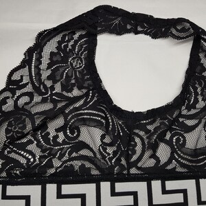 May include: Black lace halter top with intricate floral and scrollwork patterns. The top features a geometric design at the bottom in black and white. The lace is delicate and the overall design is elegant.