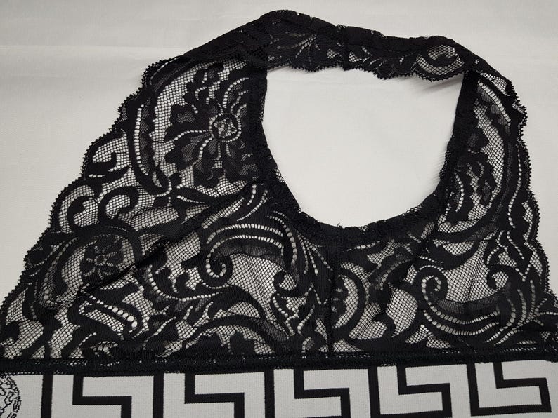 May include: Black lace halter top with intricate floral and scrollwork patterns. The top features a geometric design at the bottom in black and white. The lace is delicate and the overall design is elegant.