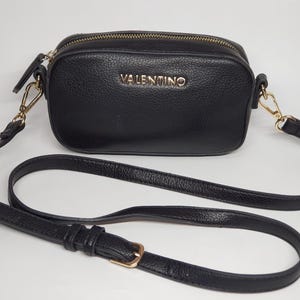 Pu&ograve; includere: Borsa a tracolla nera con cerniera dorata e tracolla lunga e regolabile. La borsa presenta il nome del marchio "VALENTINO" in lettere dorate sul davanti. La borsa &egrave; realizzata in materiale strutturato.