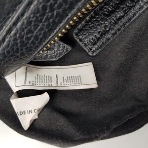 Pu&ograve; includere: Primo piano di una borsa in pelle nera con cerniera dorata. L'interno della borsa &egrave; visibile, insieme a un'etichetta che dice "MADE IN CH". La borsa ha una superficie strutturata.
