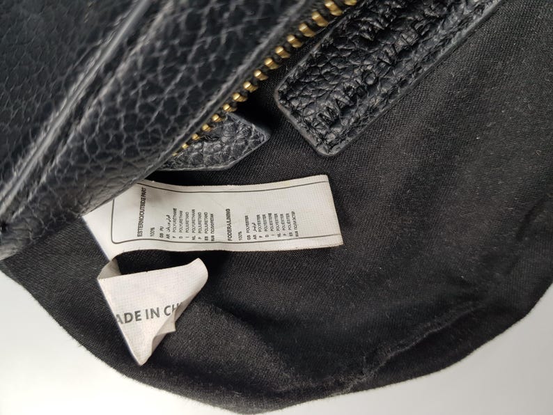 Pu&ograve; includere: Primo piano di una borsa in pelle nera con cerniera dorata. L'interno della borsa &egrave; visibile, insieme a un'etichetta che dice "MADE IN CH". La borsa ha una superficie strutturata.