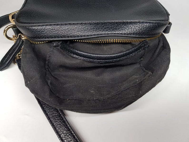 Pu&ograve; includere: Borsa a tracolla nera con esterno strutturato e cerniera dorata. La borsa ha un piccolo manico e una lunga tracolla. L'interno &egrave; in tessuto nero. La borsa &egrave; su una superficie bianca.