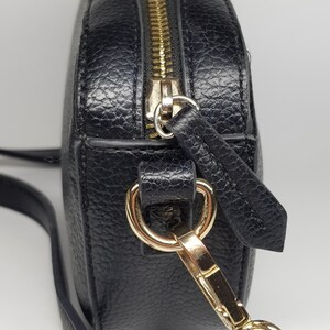 Pu&ograve; includere: Borsa a tracolla nera con finitura strutturata. La borsa presenta una cerniera e hardware color oro, tra cui una chiusura e anelli per la tracolla. La tracolla &egrave; sottile e regolabile.
