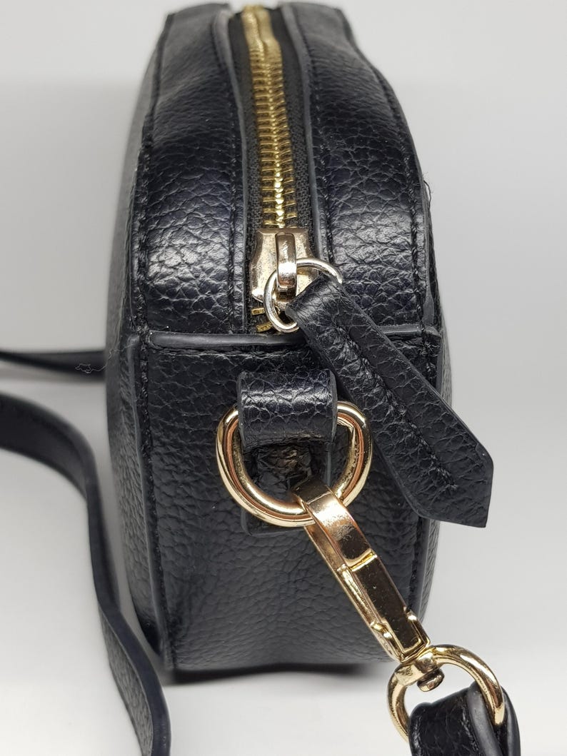 Pu&ograve; includere: Borsa a tracolla nera con finitura strutturata. La borsa presenta una cerniera e hardware color oro, tra cui una chiusura e anelli per la tracolla. La tracolla &egrave; sottile e regolabile.