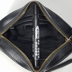Pu&ograve; includere: Borsa a tracolla in pelle nera con cerniera e hardware dorati. All'interno della borsa c'&egrave; un pennarello nero con testo bianco "AOWA". La borsa ha un piccolo manico e una lunga tracolla.