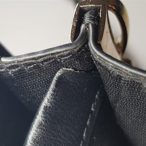 Puede incluir: Primer plano de un bolso de mano de cuero negro. La imagen destaca las costuras y un cierre met&aacute;lico dorado. El cuero parece texturizado, con costuras visibles y un acabado brillante. El dise&ntilde;o del bolso es sencillo y elegante.
