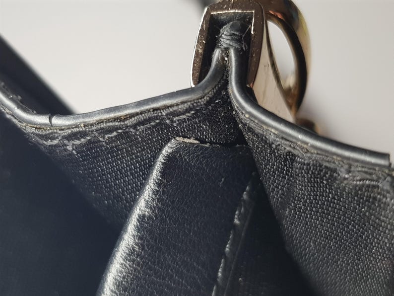 Puede incluir: Primer plano de un bolso de mano de cuero negro. La imagen destaca las costuras y un cierre met&aacute;lico dorado. El cuero parece texturizado, con costuras visibles y un acabado brillante. El dise&ntilde;o del bolso es sencillo y elegante.