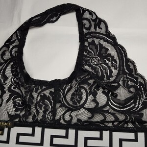 May include: Black lace halter top with intricate floral patterns. The top features a white and black geometric patterned band with the Versace logo and size 3. The top is made of a delicate, see-through lace material.