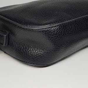 Pu&ograve; includere: Primo piano di una borsa in pelle nera con superficie strutturata. La borsa ha una forma rettangolare con angoli arrotondati e una tracolla a catena color oro. La pelle sembra essere martellata.