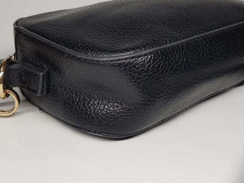 Pu&ograve; includere: Primo piano di una borsa in pelle nera con superficie strutturata. La borsa ha una forma rettangolare con angoli arrotondati e una tracolla a catena color oro. La pelle sembra essere martellata.