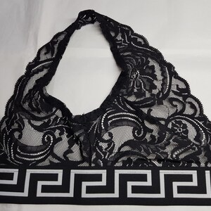 May include: Black lace halter top with a decorative pattern. The top features a black and white geometric band at the base with a Medusa head emblem. The top is designed with a halter neck and a delicate, intricate lace design.
