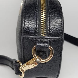 Pu&ograve; includere: Borsa a tracolla nera con cerniera e hardware color oro. La borsa ha una superficie strutturata e una lunga tracolla regolabile. La cerniera corre lungo la parte superiore. Progettata per essere indossata a spalla o a tracolla.