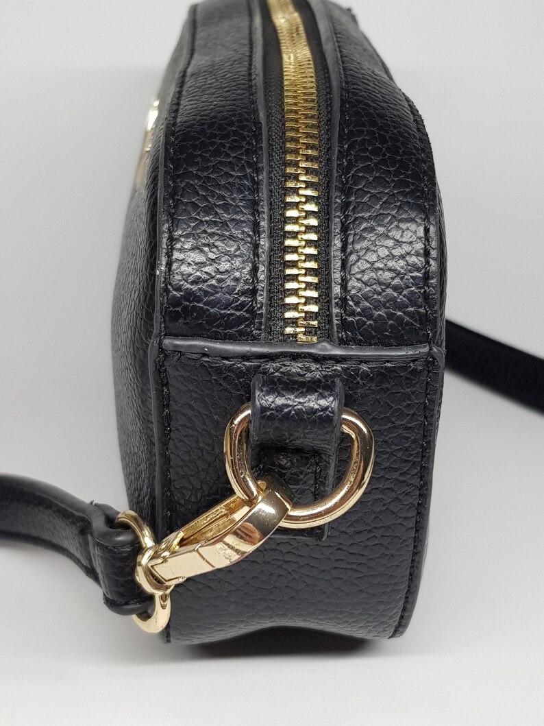 Pu&ograve; includere: Borsa a tracolla nera con cerniera e hardware color oro. La borsa ha una superficie strutturata e una lunga tracolla regolabile. La cerniera corre lungo la parte superiore. Progettata per essere indossata a spalla o a tracolla.