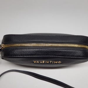 Pu&ograve; includere: Borsa a tracolla nera con cerniera dorata e il nome del marchio "VALENTINO" in lettere dorate. La borsa ha una superficie strutturata e una tracolla lunga e sottile. L'hardware &egrave; dorato.
