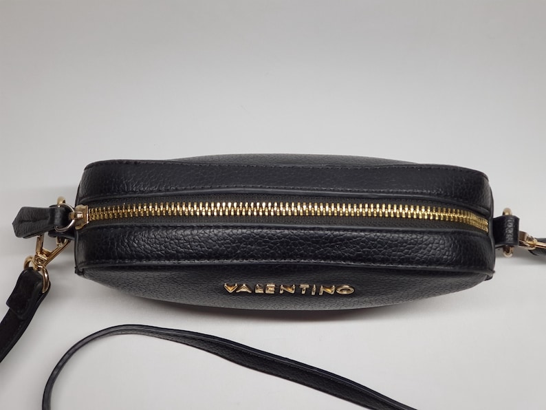 Pu&ograve; includere: Borsa a tracolla nera con cerniera dorata e il nome del marchio "VALENTINO" in lettere dorate. La borsa ha una superficie strutturata e una tracolla lunga e sottile. L'hardware &egrave; dorato.