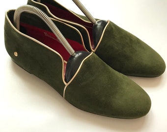 May include: A pair of green suede loafers with gold trim and a red lining. The loafers are on a white surface.