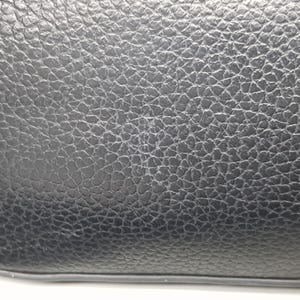 Pu&ograve; includere: Primo piano di una borsa in pelle nera con una superficie strutturata. La pelle ha una grana a grana e il bordo della borsa &egrave; visibile in basso. La borsa sembra nuova.