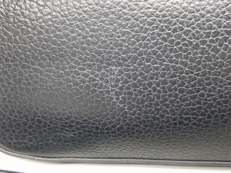 Pu&ograve; includere: Primo piano di una borsa in pelle nera con una superficie strutturata. La pelle ha una grana a grana e il bordo della borsa &egrave; visibile in basso. La borsa sembra nuova.