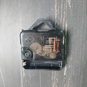 K&ouml;nnte beinhalten: Nahaufnahme der R&uuml;ckseite eines Uhrwerks mit einem schwarzen Kunststoffgeh&auml;use und einem silbernen Metallgetriebe. Die Uhr ist mit "QUARTZ" und "MADE IN CHINA" beschriftet.