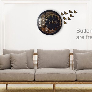 K&ouml;nnte beinhalten: Eine schwarze Uhr mit goldenem Design und einer Halbmondform. Die Uhr ist von einem Schwarm goldener Schmetterlinge umgeben. Der Text "Butterflies are free gifts" steht unter der Uhr.