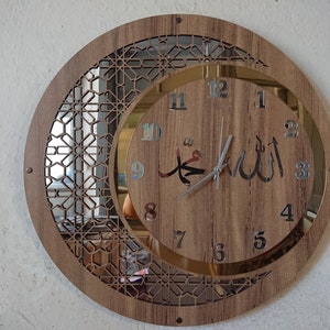K&ouml;nnte beinhalten: Eine runde Holzuhr mit einem silbernen Zifferblatt mit arabischen Ziffern und einem Halbmond-Design. Das Zifferblatt zeigt die arabischen W&ouml;rter "Allah" und "Muhammad" in silbernen Lettern.