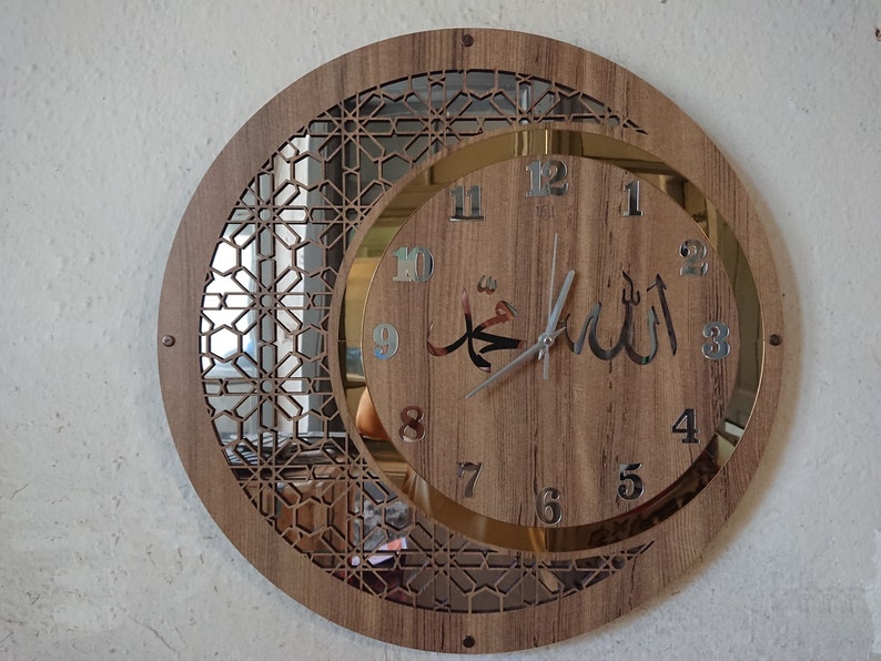 K&ouml;nnte beinhalten: Eine runde Holzuhr mit einem silbernen Zifferblatt mit arabischen Ziffern und einem Halbmond-Design. Das Zifferblatt zeigt die arabischen W&ouml;rter "Allah" und "Muhammad" in silbernen Lettern.