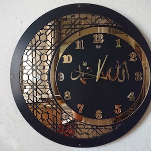 K&ouml;nnte beinhalten: Eine schwarze und goldene Uhr mit arabischen Ziffern und dem Wort "Allah" in arabischer Schrift. Die Uhr hat ein dekoratives, geometrisches Design am Rand.