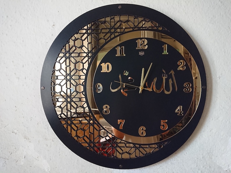 K&ouml;nnte beinhalten: Eine schwarze und goldene Uhr mit arabischen Ziffern und dem Wort "Allah" in arabischer Schrift. Die Uhr hat ein dekoratives, geometrisches Design am Rand.