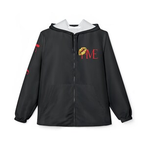 Peut inclure: Veste à capuche noire zippée avec doublure blanche dans la capuche. La veste présente le mot "TIME" en rouge, avec un motif de lèvres dorées et jaunes au-dessus de "ME". Le texte rouge est sur la manche gauche.