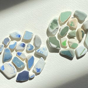 Puede incluir: Dos composiciones circulares de trozos de vidrio de mar en tonos azules, verdes y blancos. Las piezas azules están a la izquierda y las verdes a la derecha. El vidrio de mar tiene un aspecto liso y esmerilado, con formas y tamaños variados.