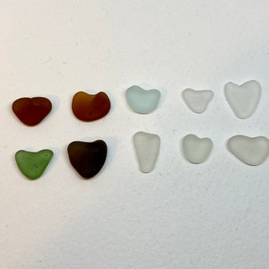 May include: Assortment of nine sea glass hearts in various colors, including brown, green, and white.