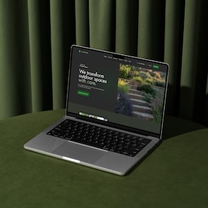 Laptop mockup displaying a landscaping Wix website template on a green table with curtain backdrop.