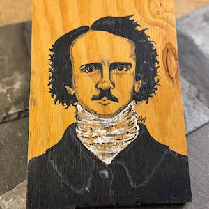 Puede incluir: Retrato pintado a mano de un hombre con cabello oscuro y bigote sobre una placa de madera. El hombre lleva un abrigo negro y un cuello con estampado blanco y dorado. El fondo es de color madera clara.