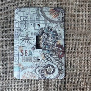 May include: A light switch cover with a steampunk design featuring a seahorse, gears, and an octopus. The cover is white with brown, blue, and orange accents. The text "SEA HORSE" is printed on the cover.