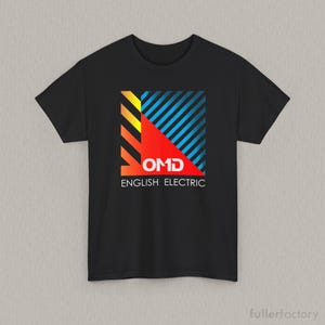 Może przedstawiać: Czarny t-shirt z krótkim rękawem z kwadratową grafiką na klatce piersiowej. Wzór zawiera ukośne żółte, pomarańczowe i niebieskie paski, czerwony trójkąt oraz biały napis OMD ENGLISH ELECTRIC wydrukowany bezszeryfową czcionką.