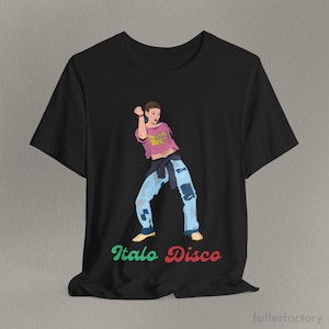 Puede incluir: Una camiseta negra de manga corta con el gráfico de una persona bailando. La figura lleva un top corto rosa con el texto Think Big en amarillo, vaqueros azules con parches y un suéter oscuro atado a la cintura. El texto Italo Disco aparece debajo.