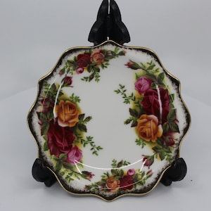 May include: A white porcelain trinket dish with a scalloped edge and a black and gold trim. The dish is decorated with a floral pattern of red, yellow, and pink roses.
