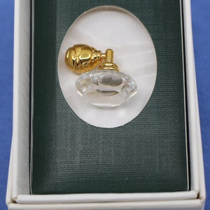 May include: A crystal perfume bottle with a gold-colored atomizer is presented in a white box with a green interior. The bottle has a faceted, diamond-like design. The atomizer is a rounded shape.