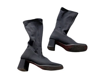 May include: A pair of black, mid-calf boots with a square toe and a block heel. The boots are made of a stretchy fabric and have a red sole. The heel height is approximately 3 inches.