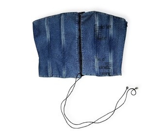 May include: A blue denim corset top with black lacing and a black drawstring. The corset has a printed design on the right side.