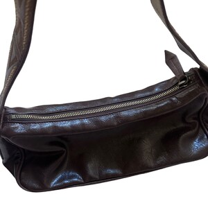 Pu&ograve; includere: Una borsa a tracolla in pelle marrone con chiusura a zip e una tracolla decorativa.