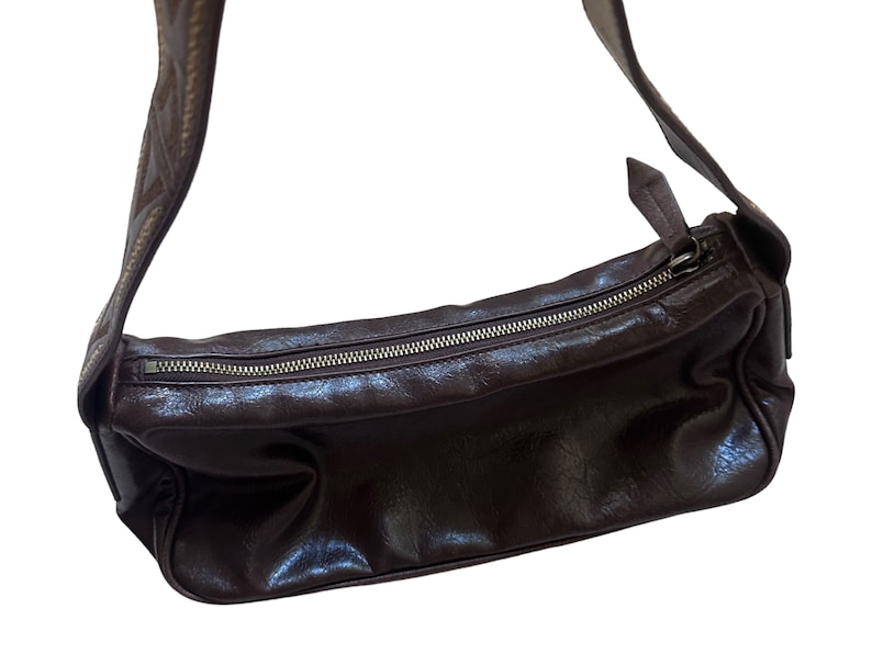 Pu&ograve; includere: Una borsa a tracolla in pelle marrone con chiusura a zip e una tracolla decorativa.