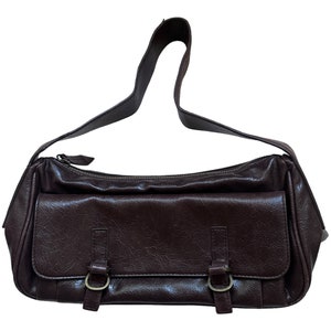 Pu&ograve; includere: Una borsa a tracolla in pelle marrone con un cinturino singolo e due fibbie sul davanti.