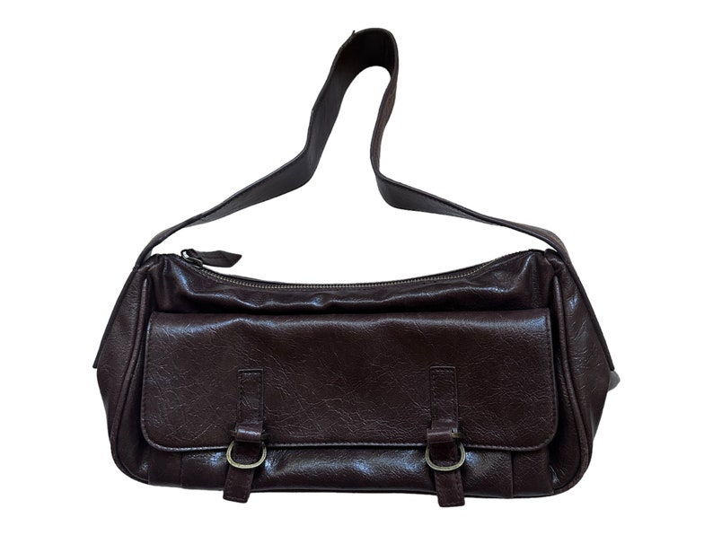 Pu&ograve; includere: Una borsa a tracolla in pelle marrone con un cinturino singolo e due fibbie sul davanti.