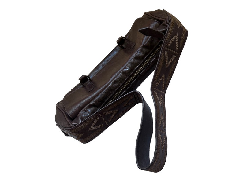 Pu&ograve; includere: Una borsa a tracolla in pelle marrone con chiusura a zip e una tracolla a fantasia. La tracolla presenta un motivo geometrico con cuciture marroni.