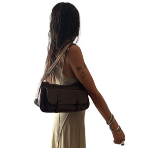 Pu&ograve; includere: Una borsa a tracolla in pelle marrone con una tracolla. La borsa ha due fibbie e una chiusura a lembo.